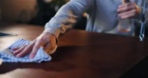 Person cleaning and caring for the surface of a dark wood dining table.